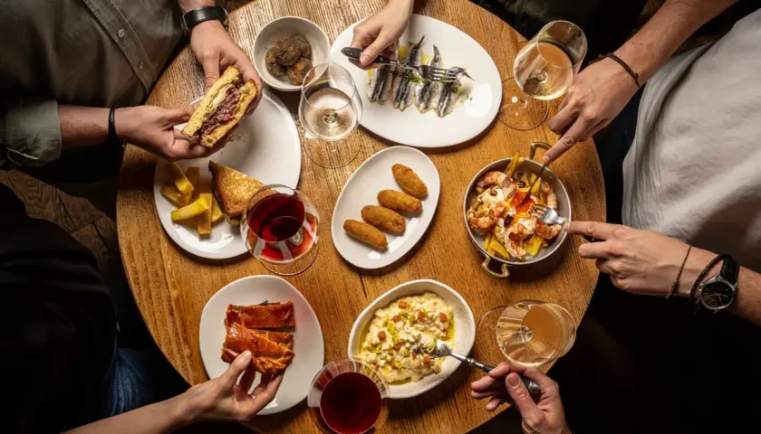 Amigos disfrutan tapas variadas: sándwich, croquetas, sardinas, gambas y pastel salado. ¡Un festín para saber donde comer bien y barato en Talavera de la Reina!