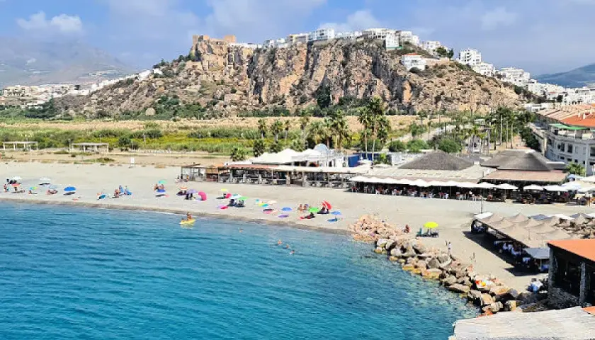 Vista de las playas de Salobreña con gente disfrutando del sol y el mar. El castillo de Salobreña corona la colina.