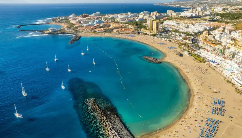 Vista aérea de una bahía con aguas turquesas, veleros y una playa repleta de gente, un ejemplo de las mejores playas Tenerife.