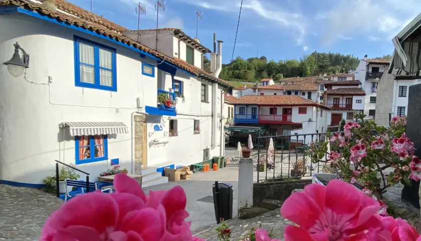 Casas blancas con detalles azules, tejados rojos y flores rosadas en un día soleado. Un vistazo a los encantadores pueblos cerca de Cudillero.