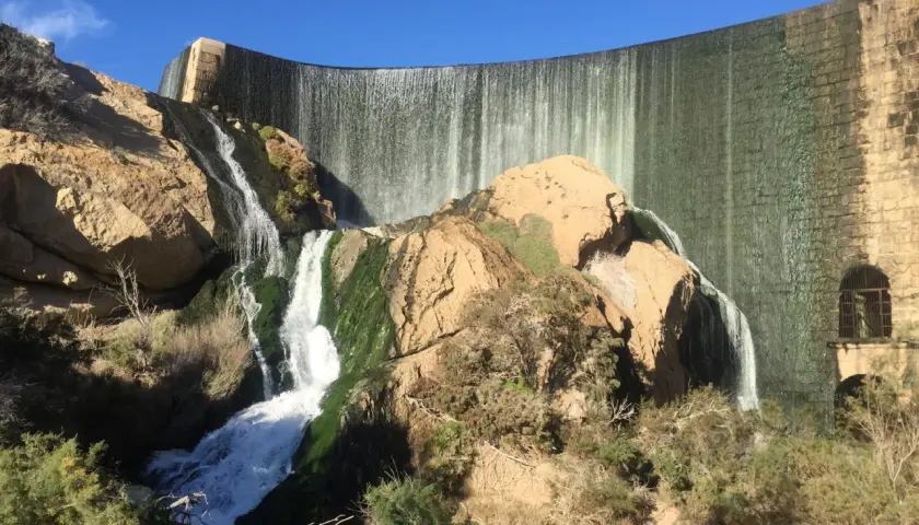 Cascada en la presa de Elche, un lugar ideal para una ruta pantano elche. El agua cae sobre rocas cubiertas de musgo y vegetación.