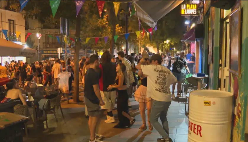 Gente disfrutando de las fiestas de San Lorenzo en Madrid, con luces, música y ambiente festivo en la calle.