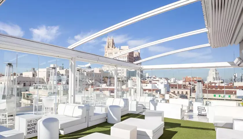 La terraza de Oscar, un oasis blanco con sofás modulares y césped artificial, ofrece vistas urbanas bajo un cielo azul.