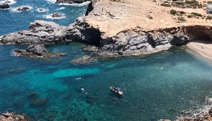 La cala Medina en Cabo de Palos, con aguas cristalinas y una pequeña embarcación, invita a explorar sus secretos.