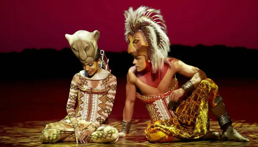 Dos actores con trajes de león, uno con máscara de leona y otro con melena, sentados en el escenario. La duración del Rey León en Madrid es inolvidable.