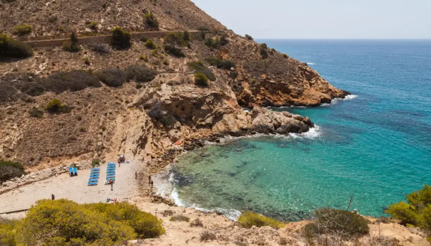 La cala Tío Ximo, con sus aguas turquesas y rocas doradas, invita a relajarse bajo el sol.