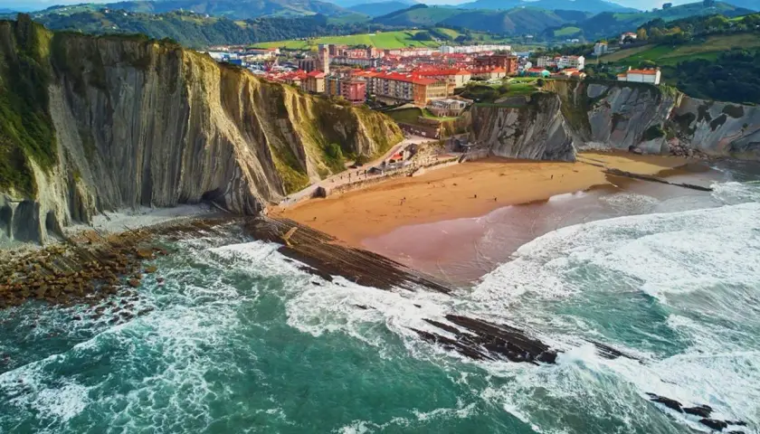 Impresionantes paisajes del País Vasco: acantilados, playa dorada y el mar Cantábrico rompiendo en rocas.