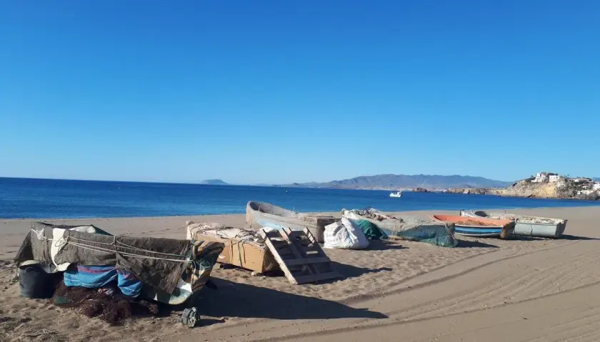 Barcas de pesca cubiertas en la arena de las playas de Mazarrón, con el mar azul y montañas al fondo.