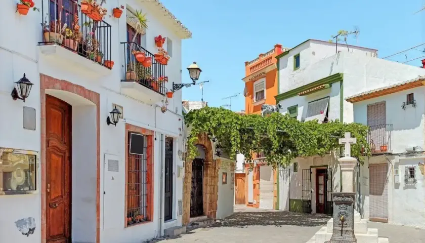Callejuela con casas blancas, balcones floridos y una fuente. Así es donde está Denia, un rincón con encanto.