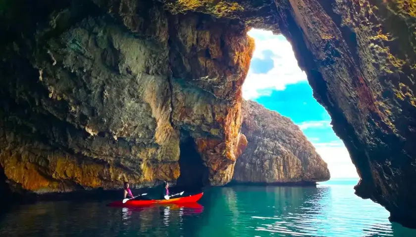 Dos personas en kayak exploran la Cova del Llop Mari en Jávea, con aguas turquesas y formaciones rocosas impresionantes.