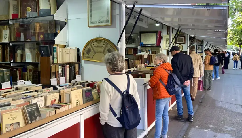 Gente buscando tesoros literarios en la feria del libro antiguo de Madrid. Estanterías repletas de tomos esperan ser descubiertos.