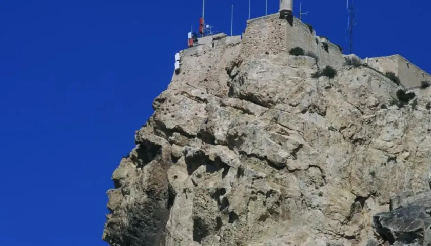 La cara del moro alicante, una roca con forma de perfil humano, corona la cima de una montaña rocosa con un castillo y una bandera española.