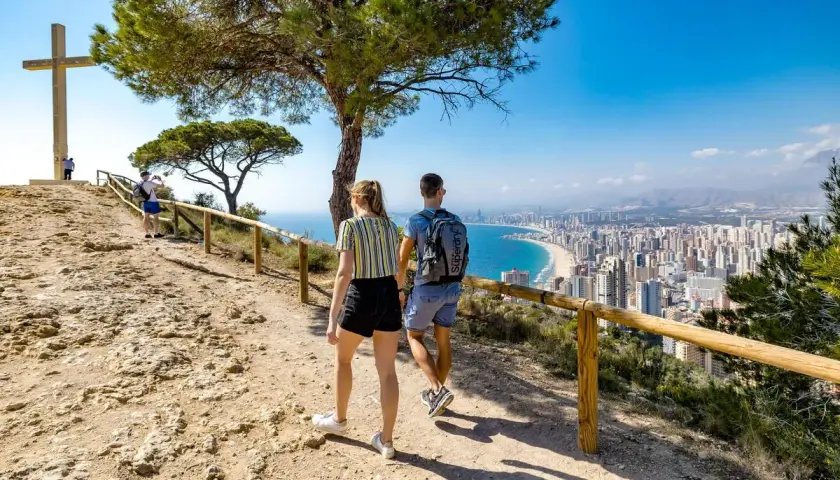 Pareja camina hacia la Cruz de Benidorm, con vistas a la ciudad y la playa.