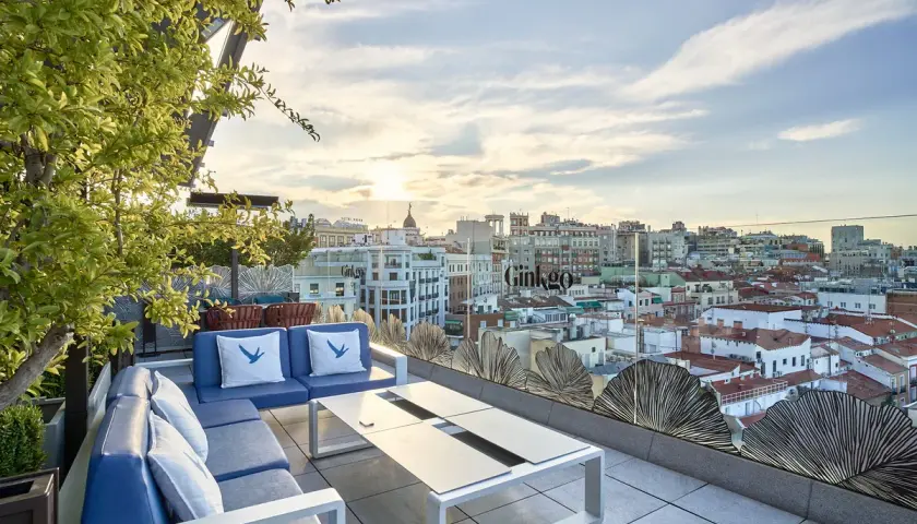 Terraza del Ginkgo restaurante & sky bar con vistas a la ciudad al atardecer. Sofás azules y mesa de centro.