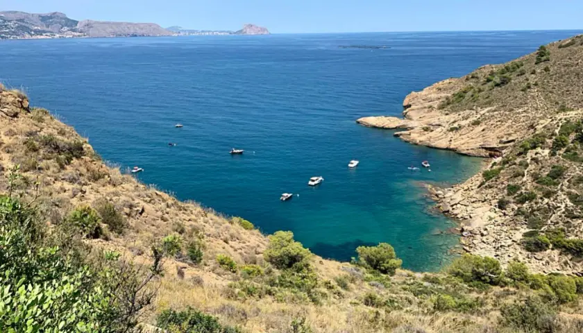 Vista panorámica de la cala de la mina, con aguas turquesas y barcos navegando.