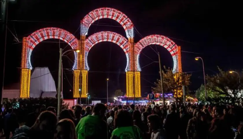 Noche de luces y alegría en las fiestas de Boadilla del Monte. Arcos luminosos decoran la entrada a un evento multitudinario.