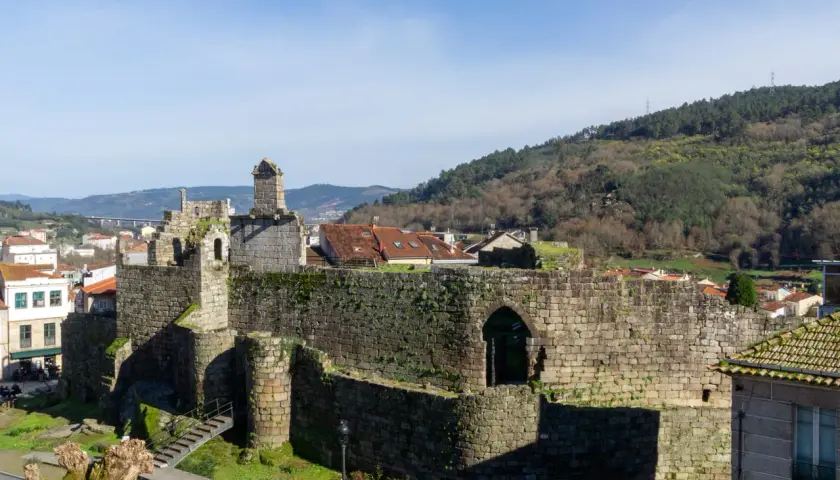 Ruinas de un castillo de piedra, con tejados rojos y colinas verdes al fondo. Un ejemplo de los pueblos bonitos cerca de Monforte de Lemos.
