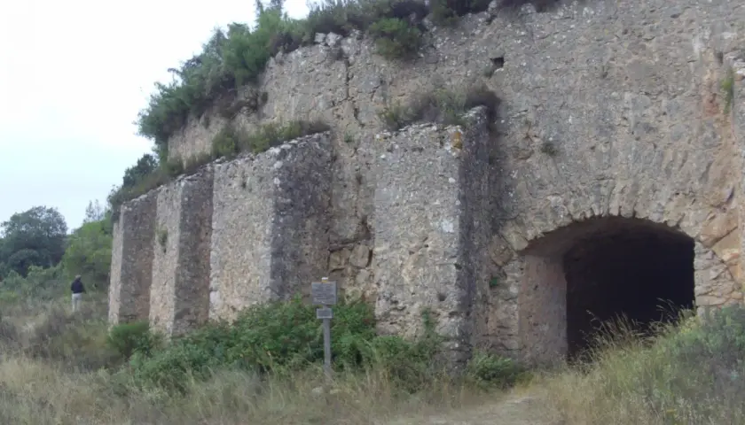 Antigua construcción de piedra en la Serra de Mariola, con un arco de entrada y vegetación circundante.