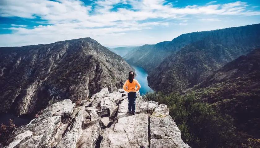 Niña en el mirador de Vilouxe, contemplando un cañón con un río azul y montañas verdes bajo un cielo nublado.
