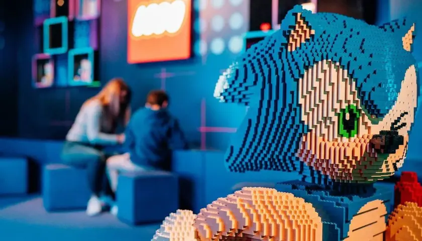 Figura de Sonic hecha de LEGO en el museo LEGO de Madrid. Al fondo, dos personas observan una exposición.