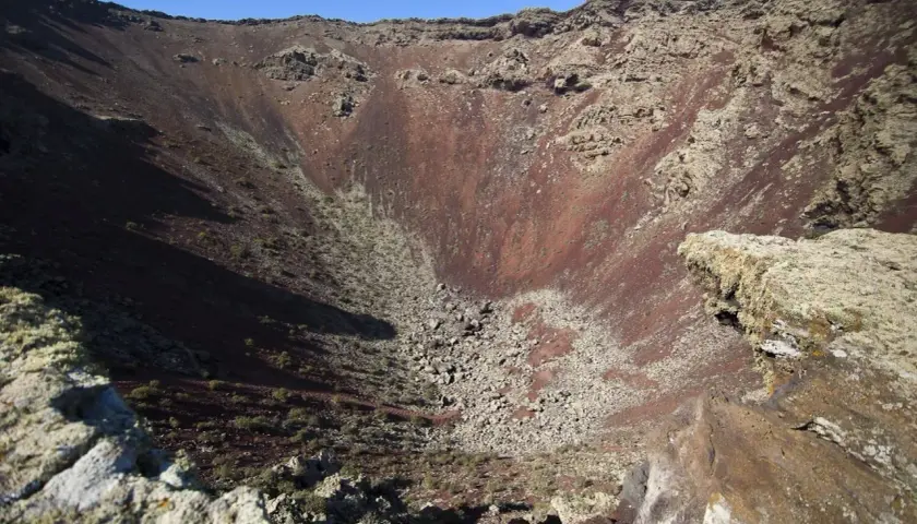 Interior del cráter del Volcán de la Corona, con rocas rojizas y vegetación escasa.