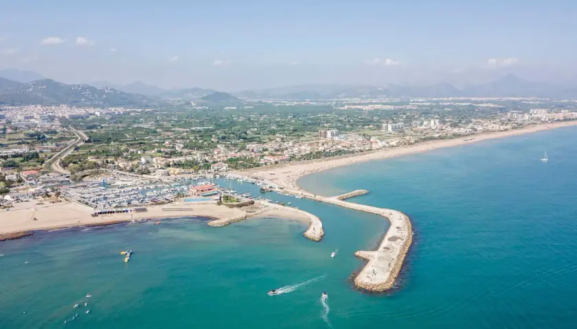 Vista aérea de la playa de Oliva, con su puerto deportivo, arena dorada y aguas turquesas. Las opiniones sobre la playa de Oliva son muy positivas.