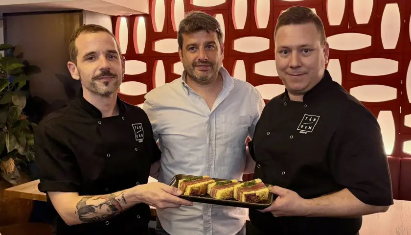 Tres hombres posan con un plato de aperitivos en un mesón. Las fotos capturan el momento.