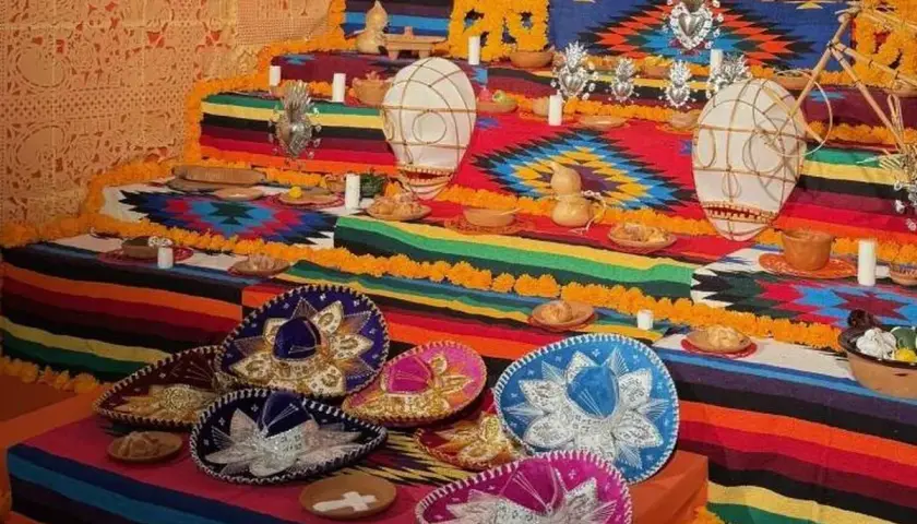 Un vibrante altar de los muertos en una casa de México, adornado con sombreros, flores de cempasúchil y ofrendas.