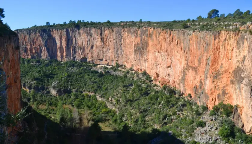 Impresionante pared rocosa anaranjada en la ruta de los calderones Chulilla, con vegetación verde cubriendo el fondo del cañón.