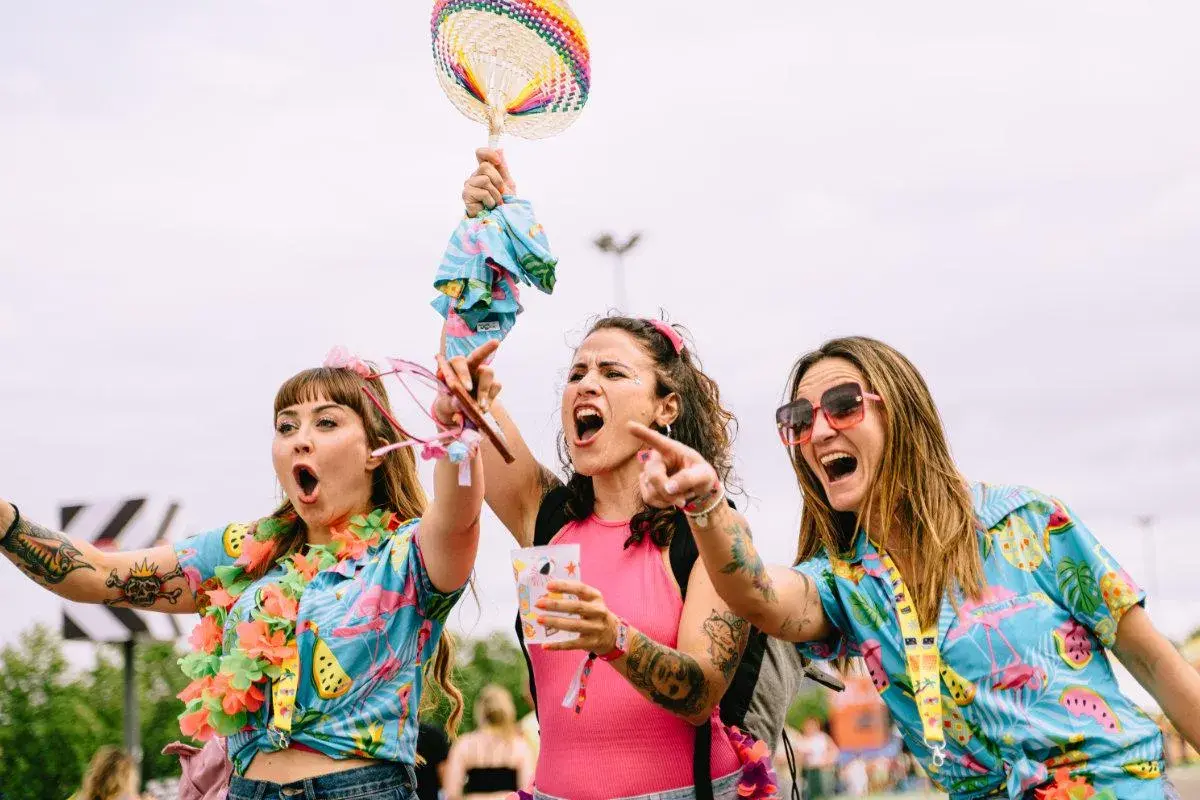 Tres chicas con camisas tropicales y collares de flores, riendo y bailando. ¡Me encanta el espíritu de las tuenti's!
