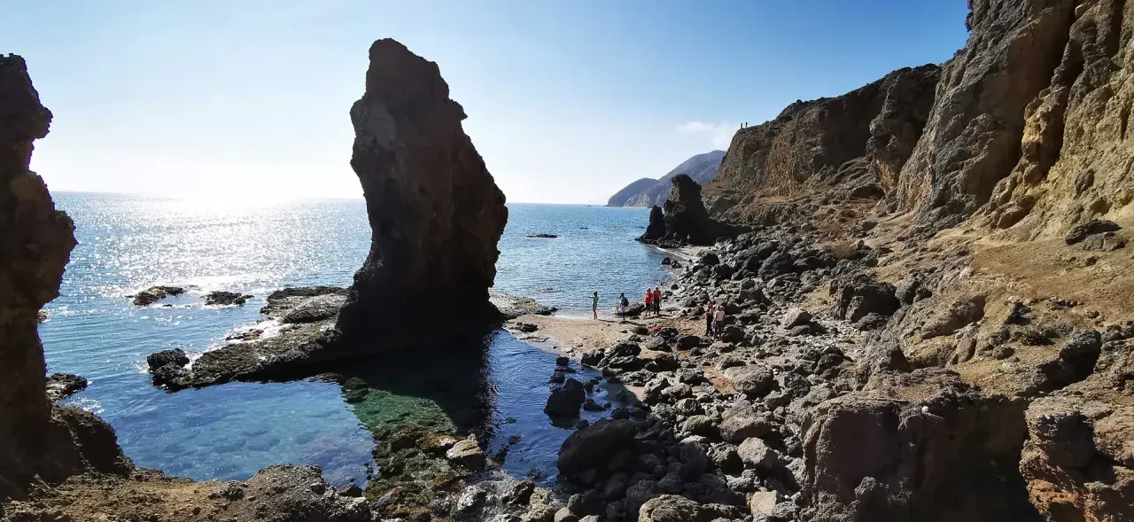 Gente disfrutando de la **playa del Sombrerico**, con sus rocas y aguas cristalinas. ¡Un lugar para guardar en la memoria!
