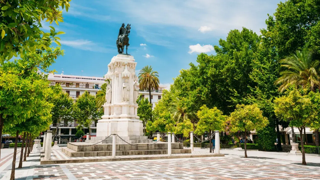 Majestuoso monumento ecuestre, una de las **estatuas en Sevilla**, rodeado de árboles frondosos y un cielo azul vibrante.