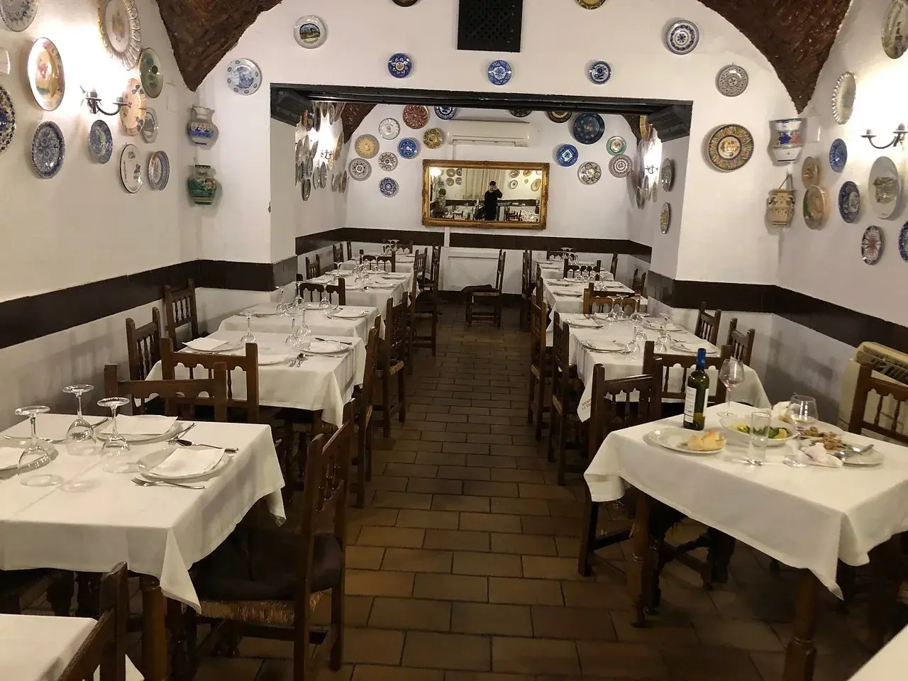 Mesas puestas en el restaurante La Troya Trujillo, decorado con platos de cerámica en las paredes.