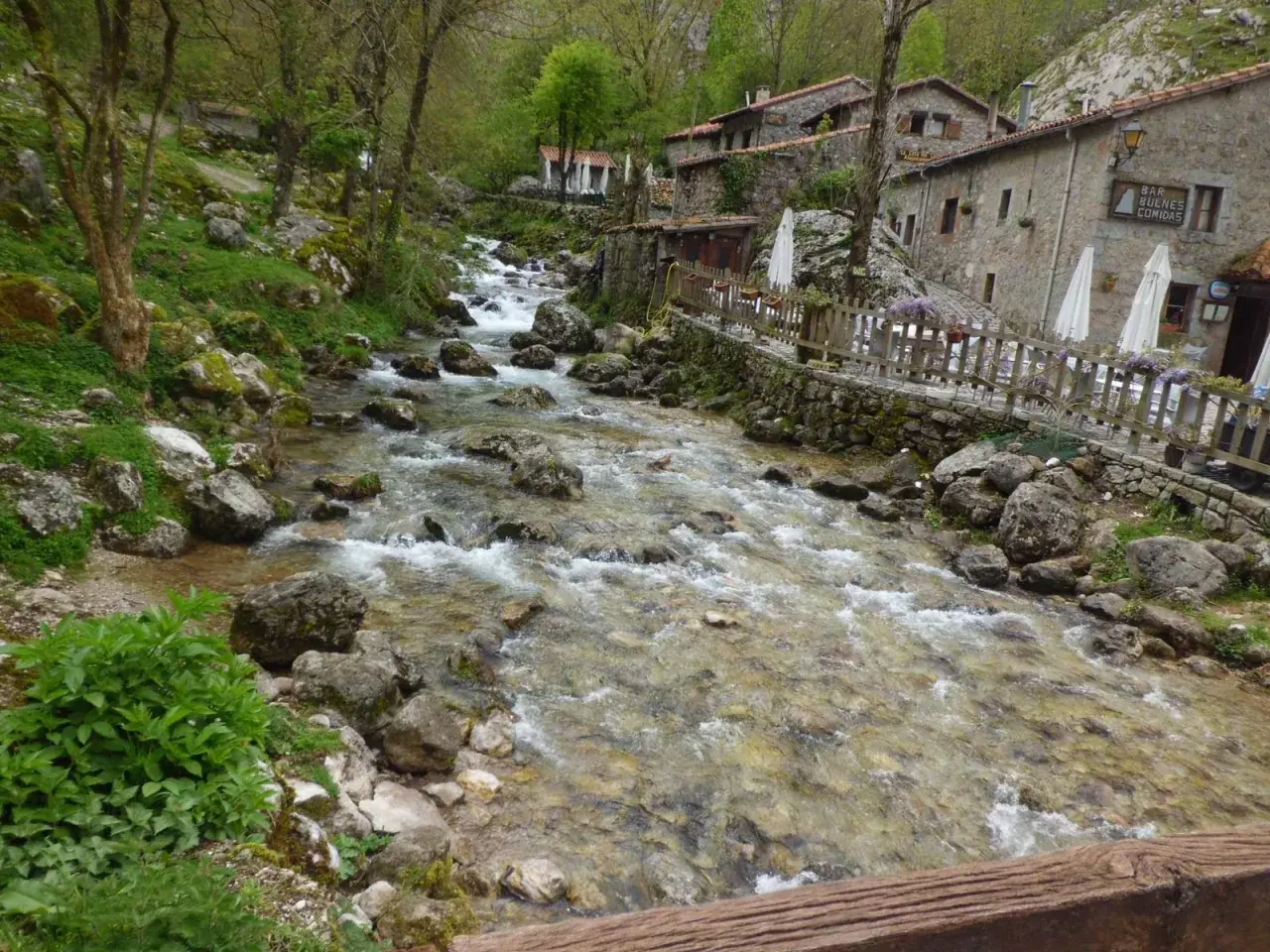 Río caudaloso y rocoso fluye hacia un pueblo de piedra con un cartel que dice "Bar Bulnes Comidas". ¡Así se llega a Bulnes!