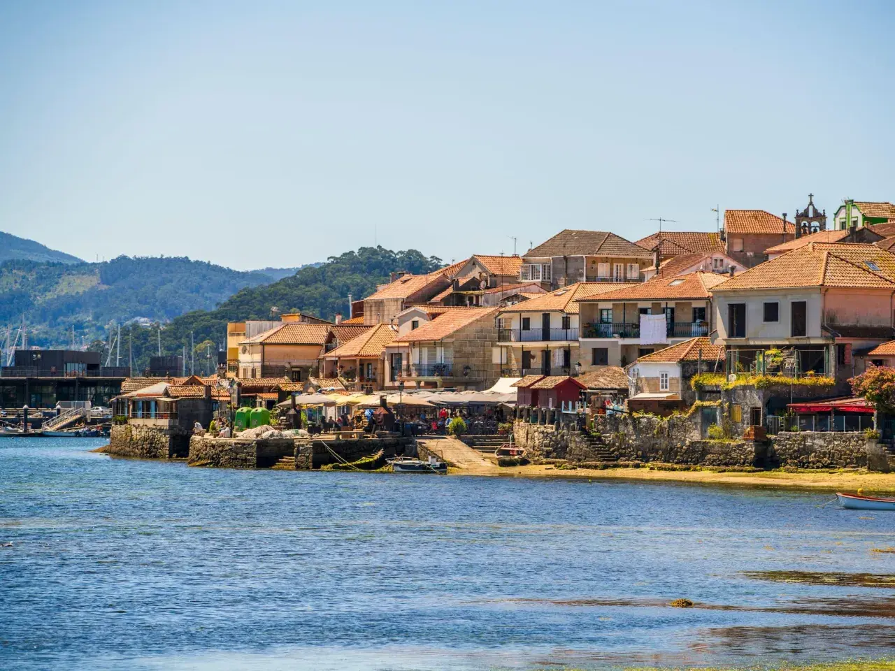 Pueblos de las Rías Baixas con casas de tejados naranjas junto al mar azul, un día soleado.