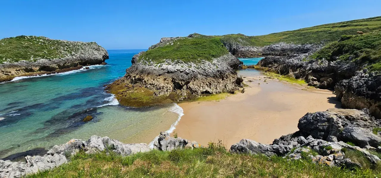 Una cala asturiana con aguas turquesas y arena dorada, rodeada de acantilados verdes. Un paraíso entre las playas más bonitas de Asturias.