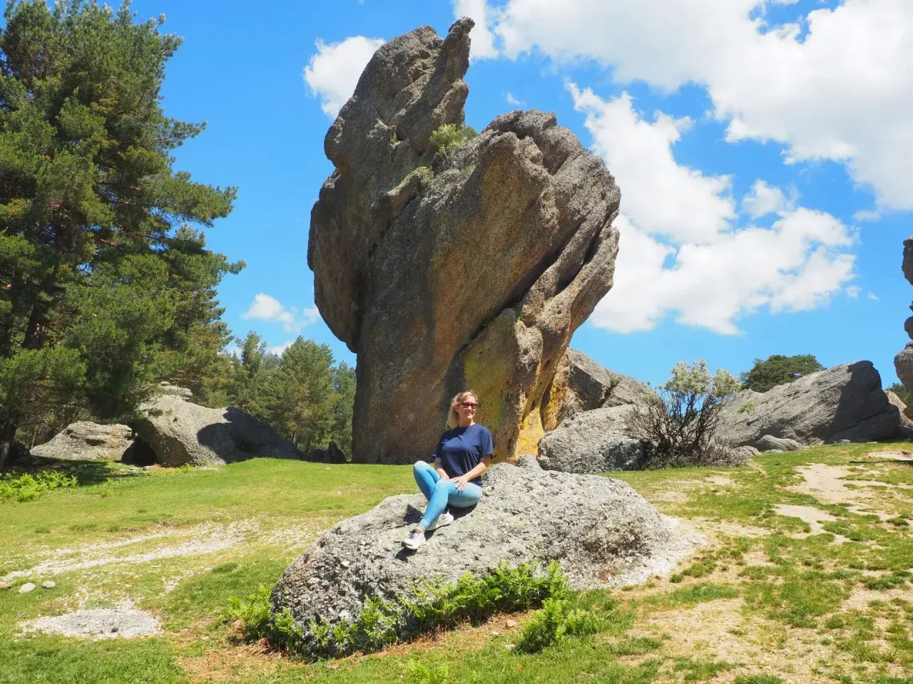 Una mujer sonríe sentada en una roca en un paisaje rocoso y verde. ¡Un lugar increíble que ver en Soria!