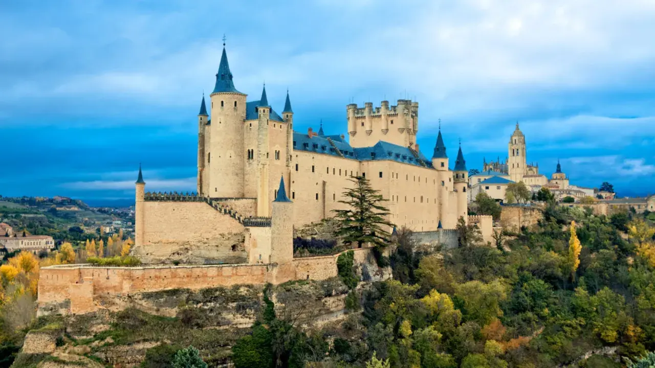 El Alcázar de Segovia, un castillo de cuento, es un imprescindible que ver en Segovia. Sus torres y murallas se alzan majestuosas sobre un paisaje otoñal.