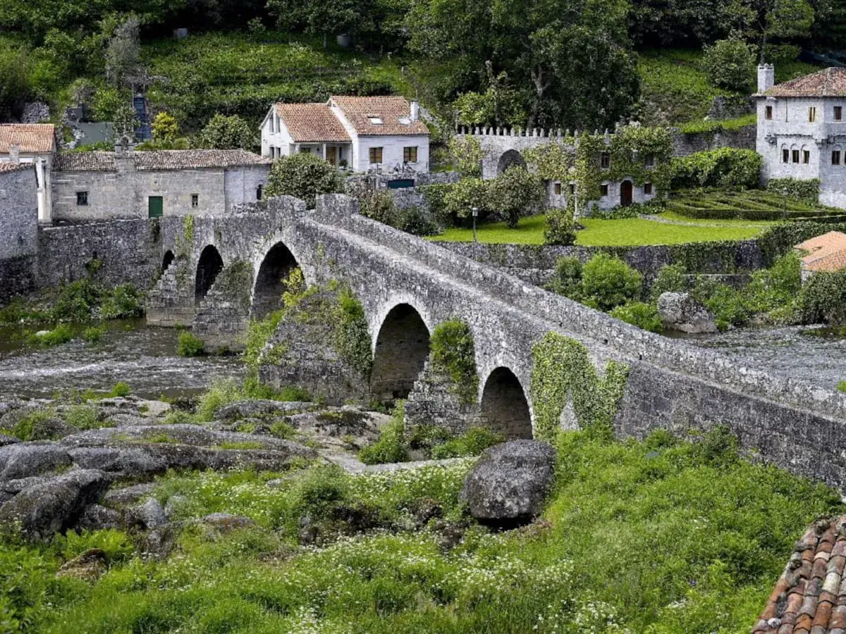 Puente de piedra cubierto de hiedra, con casas tradicionales al fondo. Un lugar idílico para visitar, así es como ponte Maceira como llegar.