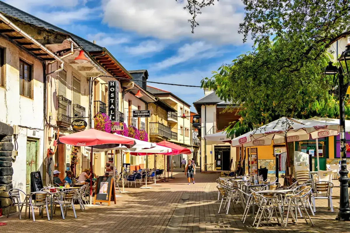 Calle con terrazas de restaurantes en pueblos cerca de León. Hostal La Gallega y Coca-Cola visibles.