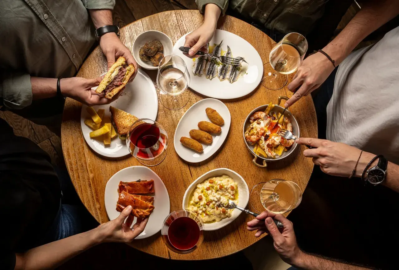Amigos disfrutan tapas variadas: sándwich, croquetas, sardinas, gambas y pastel salado. ¡Un festín para saber donde comer bien y barato en Talavera de la Reina!