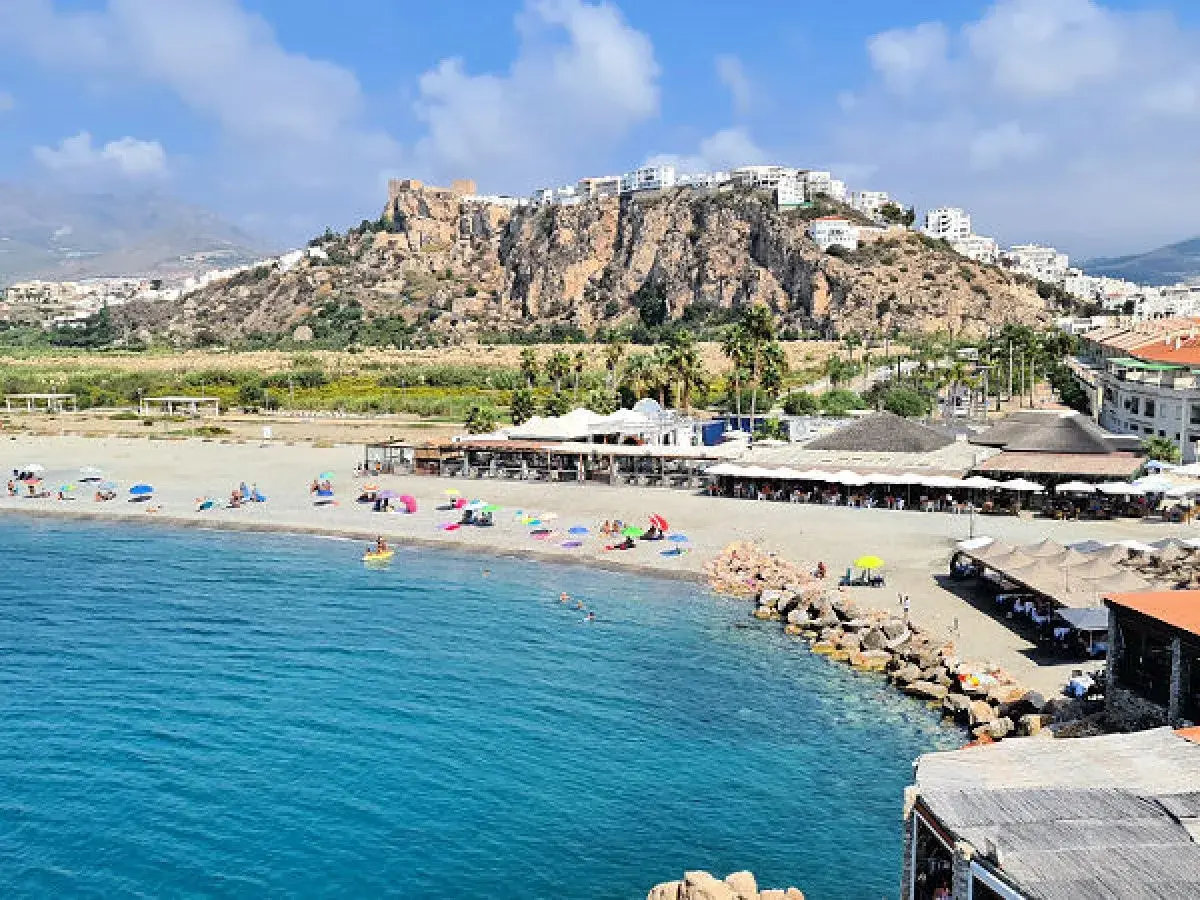 Vista de las playas de Salobreña con gente disfrutando del sol y el mar. El castillo de Salobreña corona la colina.