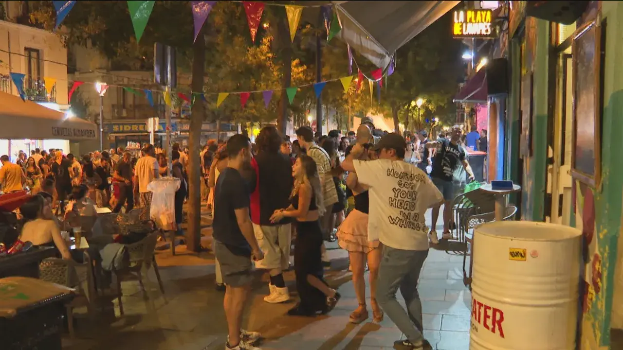 Gente disfrutando de las fiestas de San Lorenzo en Madrid, con luces, música y ambiente festivo en la calle.