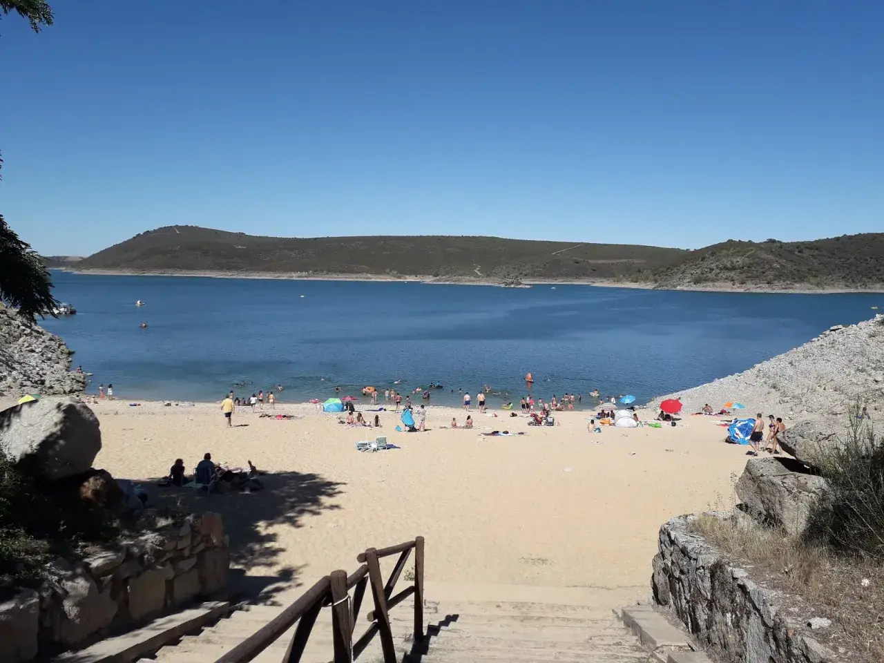 Gente disfrutando del sol y el agua en la playa fluvial de Ricobayo, un día perfecto para refrescarse.