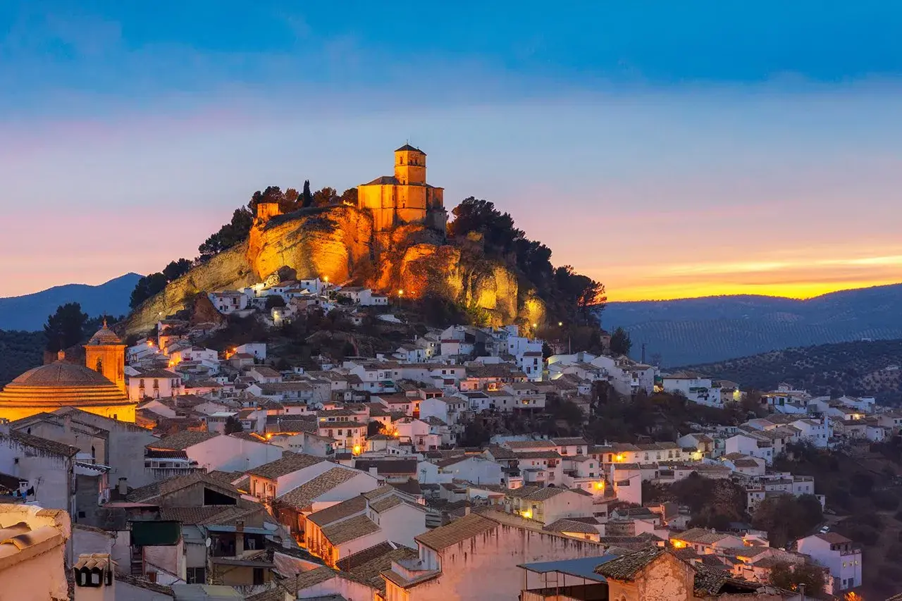 Pueblo blanco andaluz con castillo iluminado en la colina. Un lugar encantador que ver cerca de Granada al atardecer.