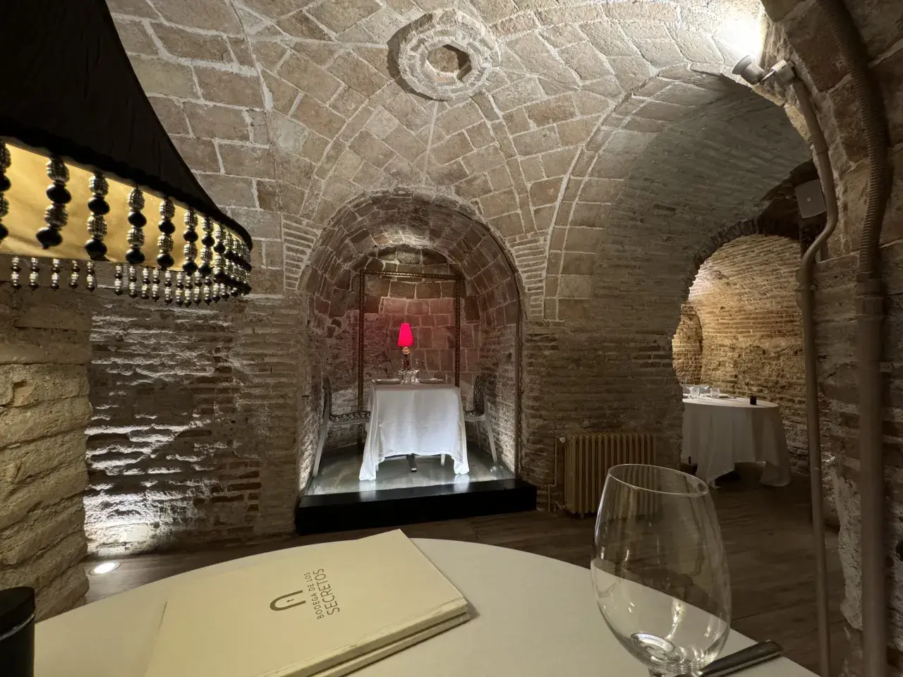 Menú de la Bodega de los Secretos en un ambiente rústico con arcos de piedra y mesas preparadas.