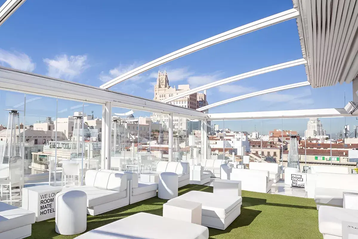 La terraza de Oscar, un oasis blanco con sofás modulares y césped artificial, ofrece vistas urbanas bajo un cielo azul.