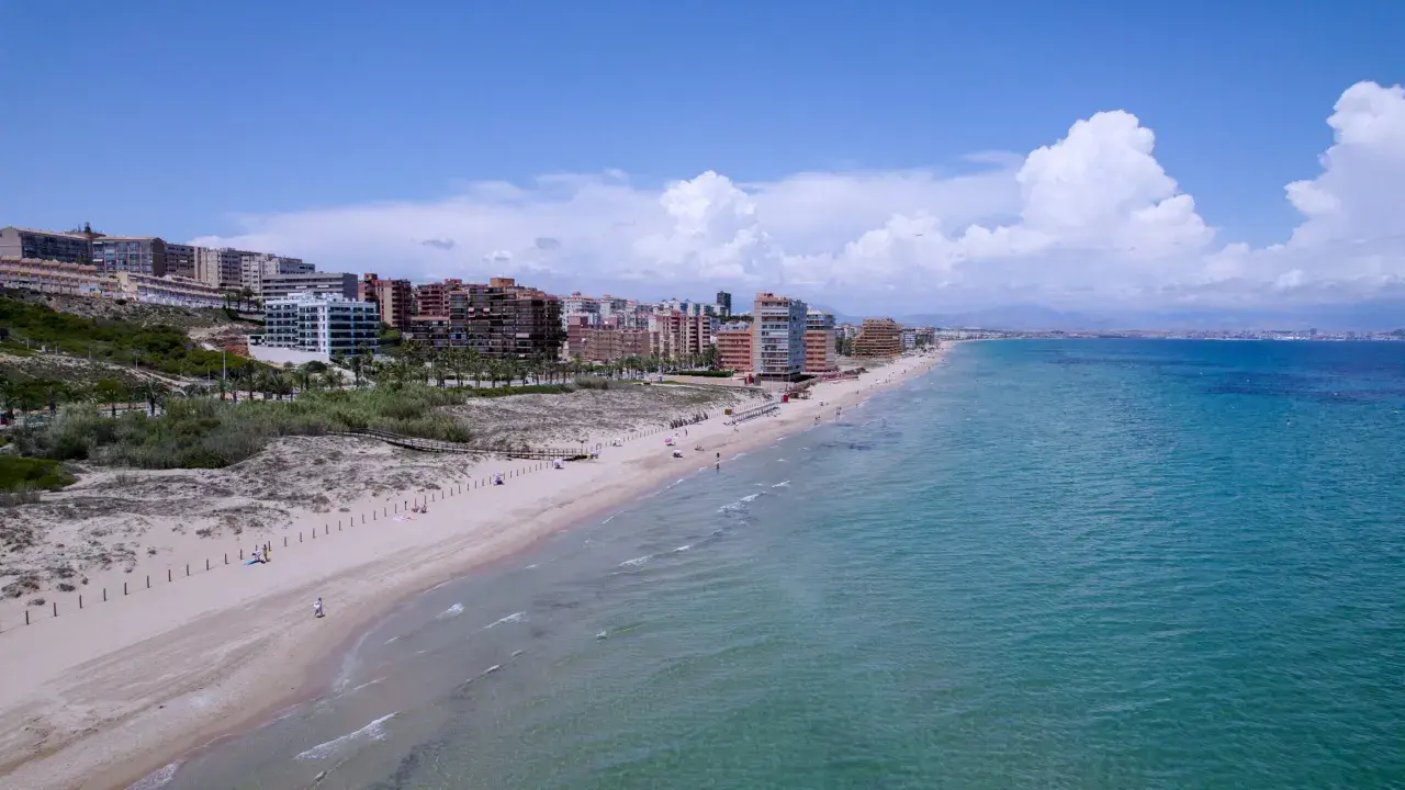 Vista aérea de la playa los Arenales con edificios residenciales al fondo y el mar turquesa.