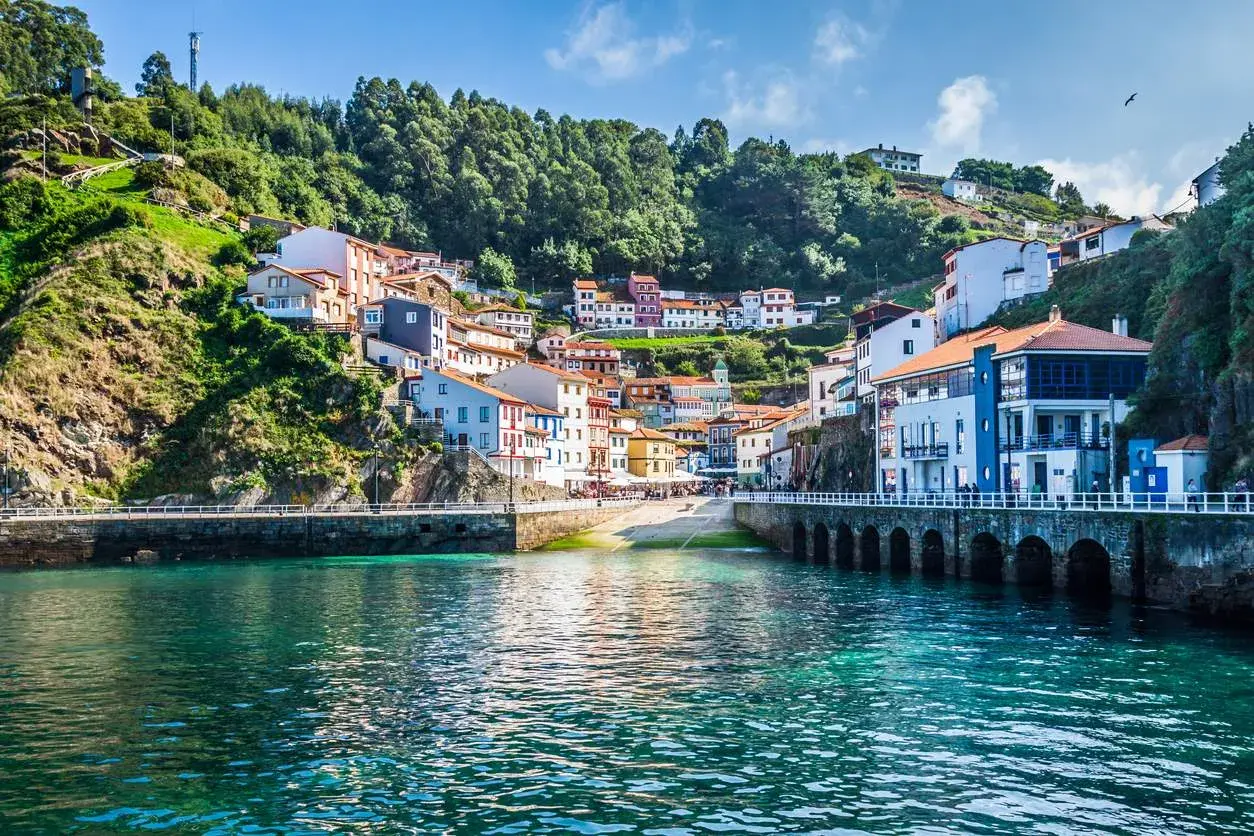 Pueblo costero con casas de colores en una ladera verde, un puerto y aguas turquesas. Un ejemplo de los lugares más bonitos de España.
