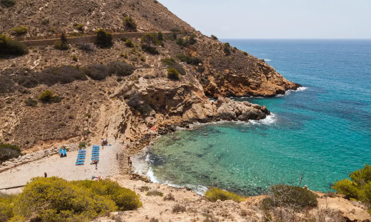 La cala Tío Ximo, con sus aguas turquesas y rocas doradas, invita a relajarse bajo el sol.
